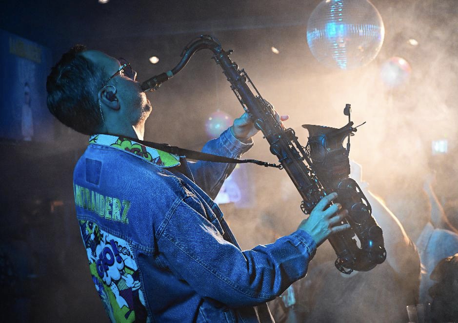 Linus Lindholm spelar saxofon i blått och varmt scenljus